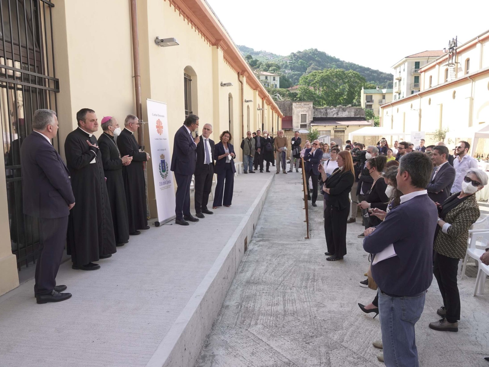 Cerimonia di consegna riconoscimento in cui 3 persone parlano di fronte al pubblico.