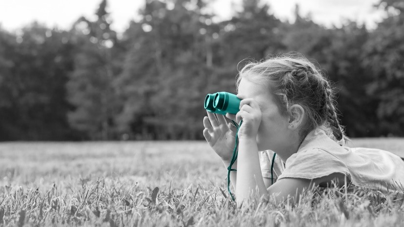 Bambina stesa su un prato che osserva il cielo con un binocolo 